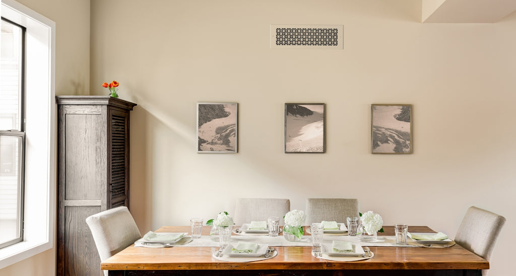 A medium close up of a wooden dining room table with a beige-painted Reggio Register cover above.