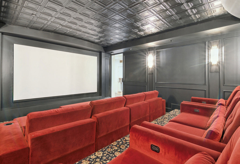 Wide view of a home theater with large screen, red velvet furnishings, and black walls with sconces.