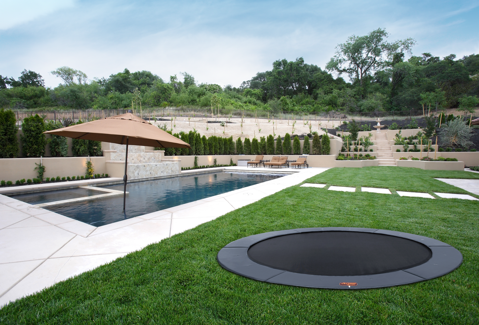 An inground trampoline in a backyard with a pool in the background