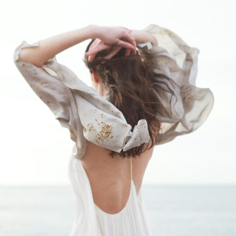 Foulard de soie biologique naturelle pour cheveux porté sur les épaules par une femme de dos devant l’océan 