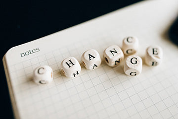 A notebook is open to a page made of graph paper and says “notes” at the top. It’s on a black background. On the open page are dice with letters are them that spell both “CHANCE” and “CHANGE,” where the “C” and “G” near the end are sharing the same space.