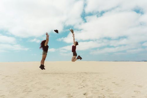 Deux femmes, sur du sable, sautent en se passant un chapeau