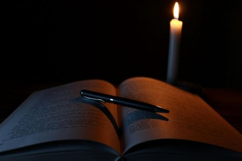 Un livre ouvert avec un stylo dessus et une bougie illumine la scène