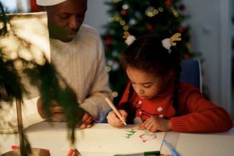 Une enfant, guidée par son papa, est en train de faire un dessin au Père Noël