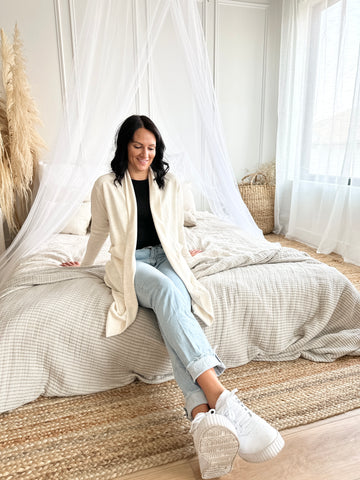 woman wearing cream cardigan and jeans sitting on a bed