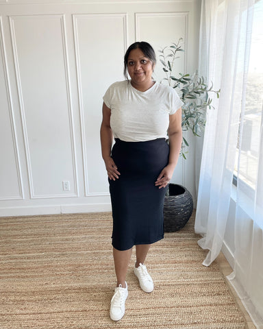 woman wearing light grey crewneck bamboo t-shirt and black midi skirt with white sneakers