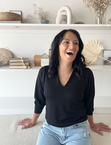 woman laughing wearing black v-neck cropped sweater and jeans
