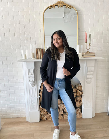 Woman wearing a black long duster cardigan and a white crewneck t-shirt with jeans and white sneakers