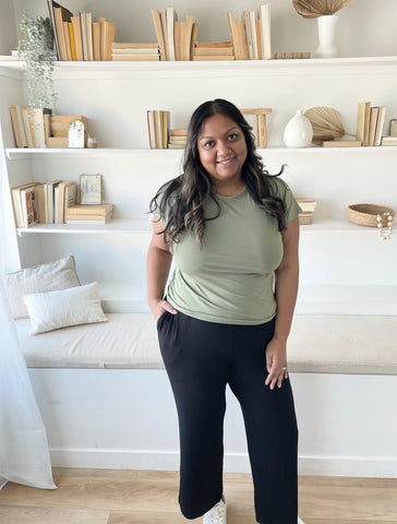 indian woman standing in front of a shelf wearing a sage green bamboo t-shirt and black wide leg pants