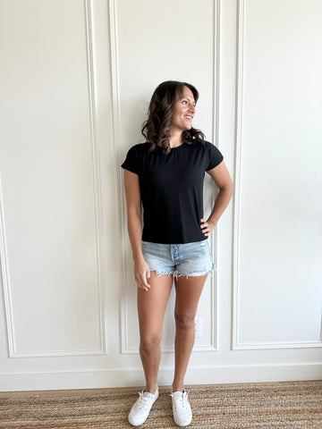 white woman standing with black crewneck t-shirt and short denim shorts