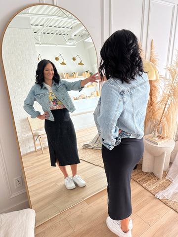 woman looking in mirror wearing black midi knit skirt with jean jacket and white sneakers