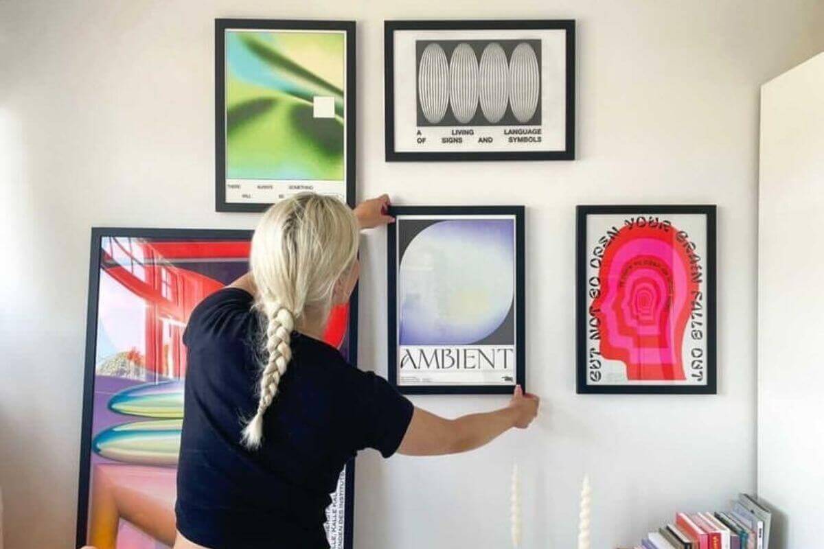 a blonde girl hanging the last artwork of a gallery wall