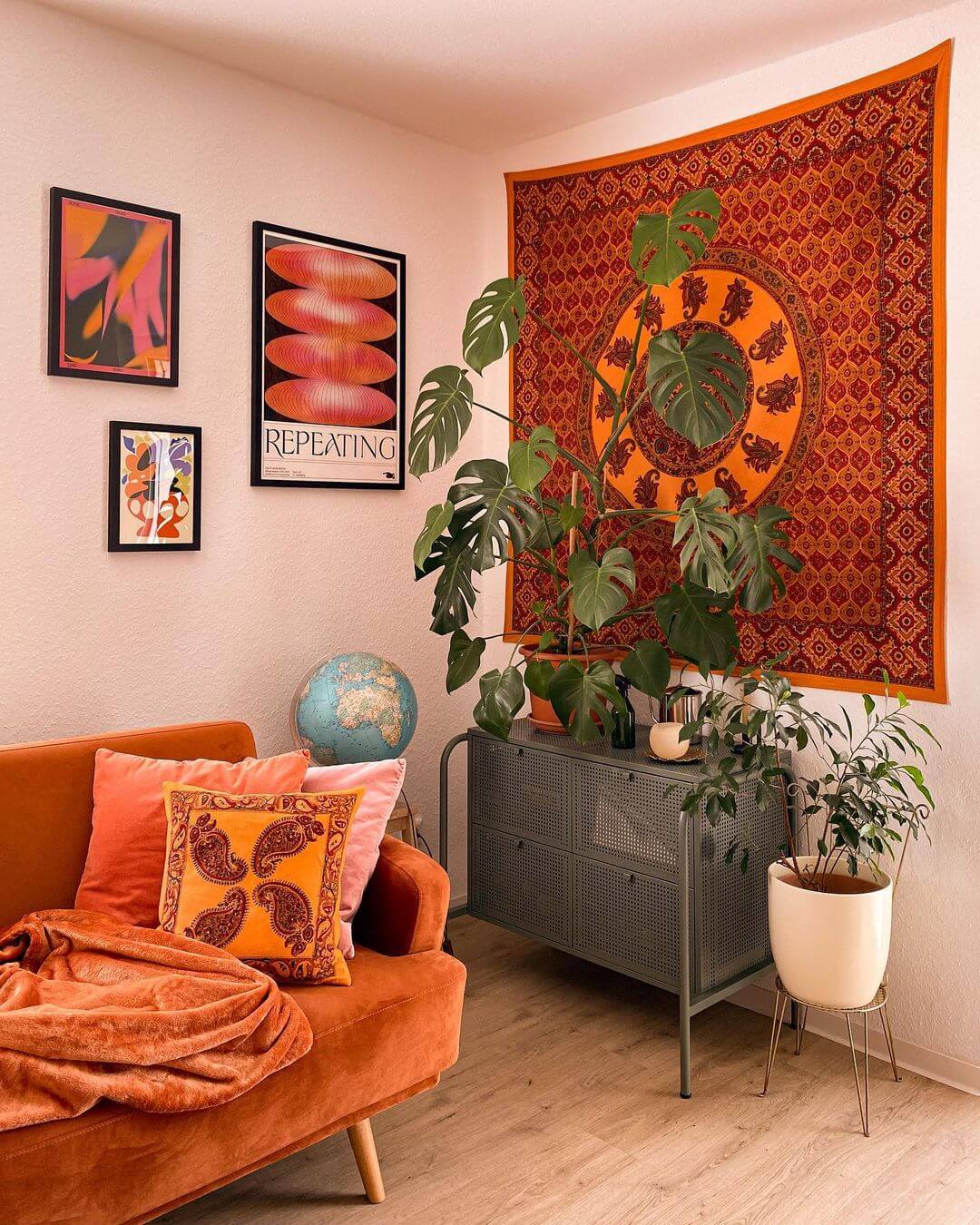 Bohemian living room with a red and orange wall hanging, orange sofa and 3 artworks hung as a gallery wall