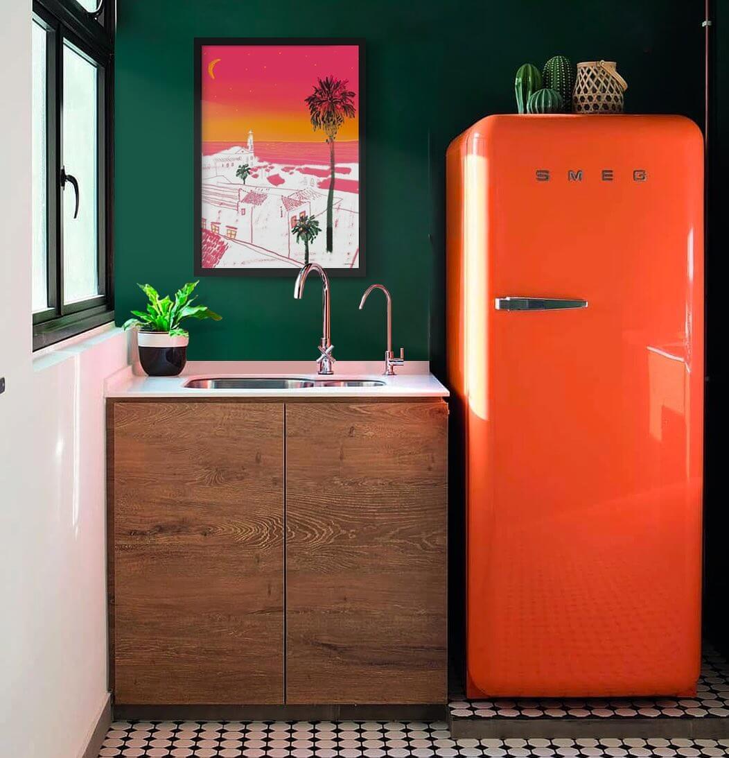 eclectic kitchen with a bright orange Smeg oven, a matching orange illustration artwork hung against a dark green painted wall