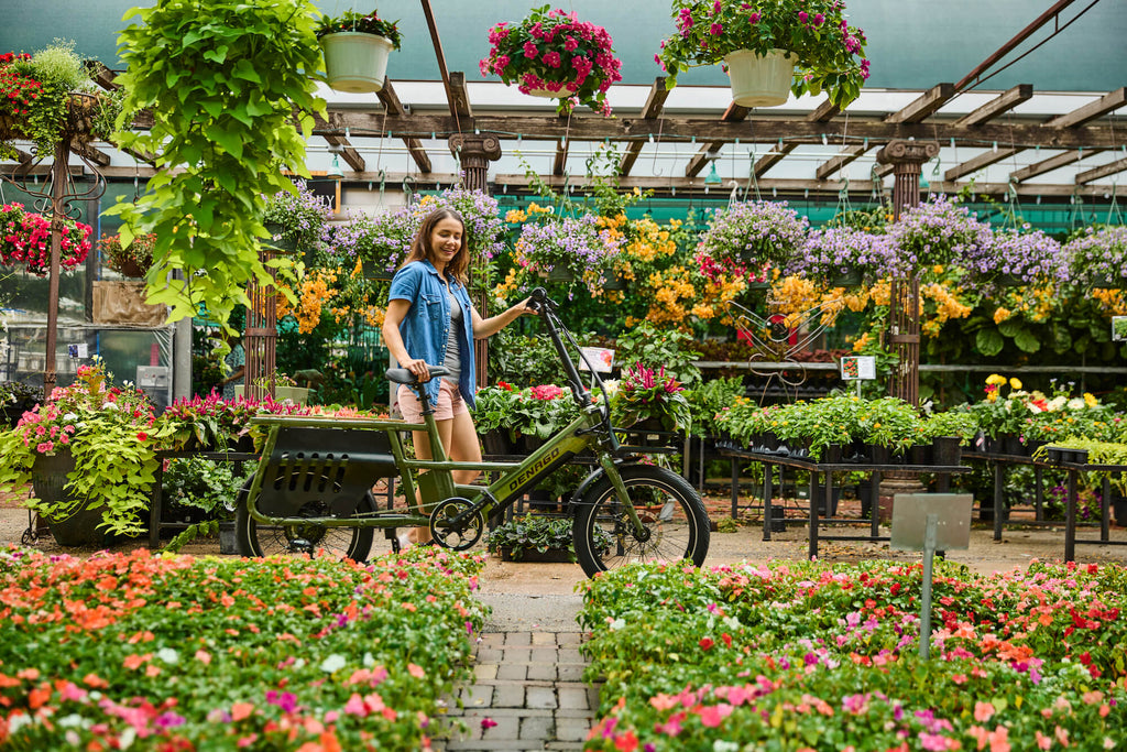 A woman shopping for garden plants among flowers while walking with the Denago Cargo 1 electric bike.