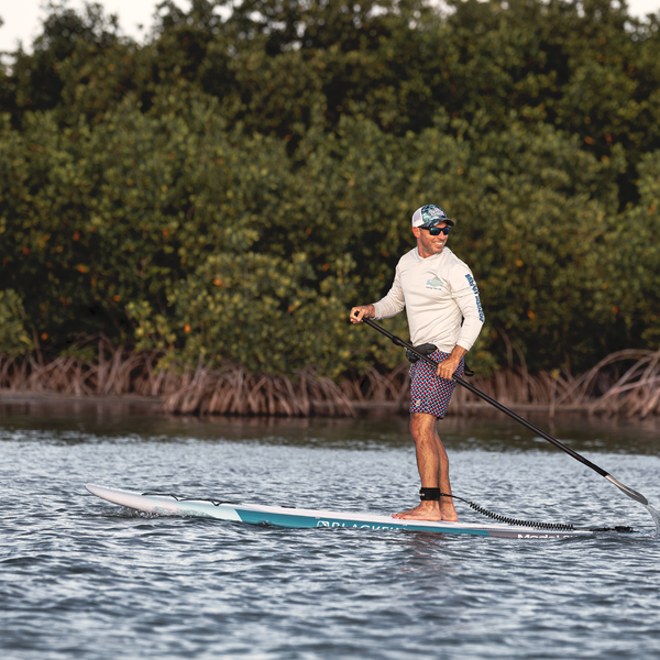 Woman carrying BLACKFIN standup paddle board on rocky shoreline