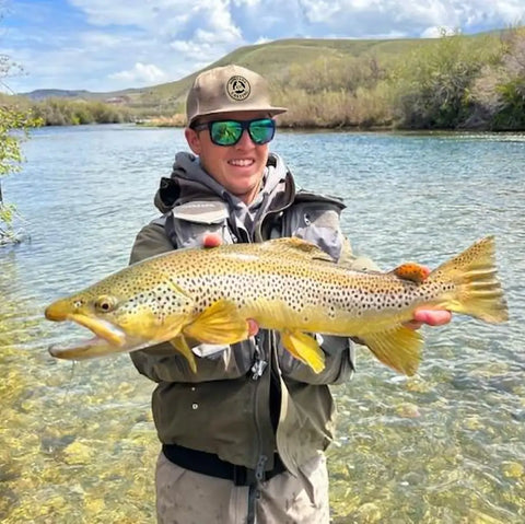 Fly fisherman holds up a brown trout.