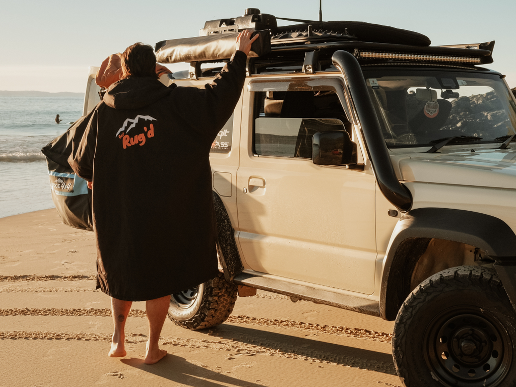 Get Rug'd HydroCloak Changing Robe and Hooded Towel Poncho worn by a man standing in front of a 4wd vehicle at the beach.