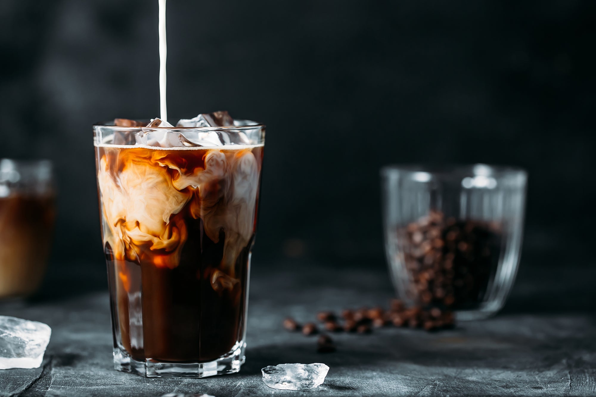 Glass with iced coffee and cream pouring in from above