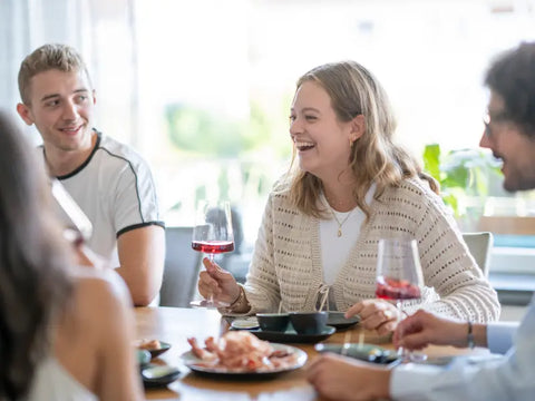 An einem mit Tapas gedeckten Tisch sitzen eine Frau und daneben zwei Männer und trinken Wein