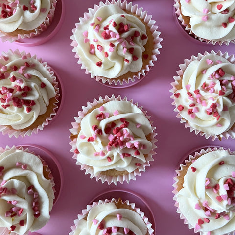 Vanilla valentines cupcakes with pink and red heart sprinkles on a pink tray