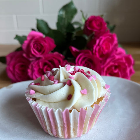 Valentines cupcake in a pink stripey cupcake case with roses in the background