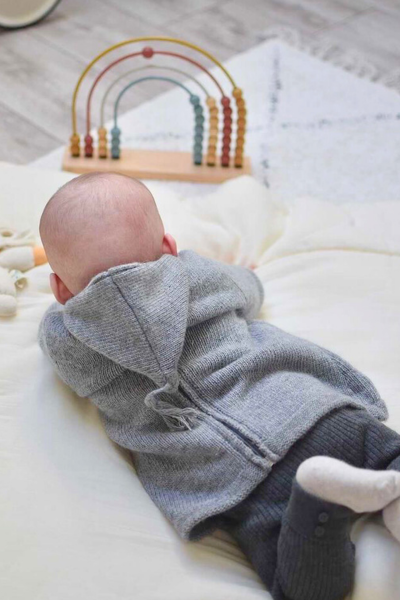 Bébé qui porte un burnous gris allongé sur un lit
