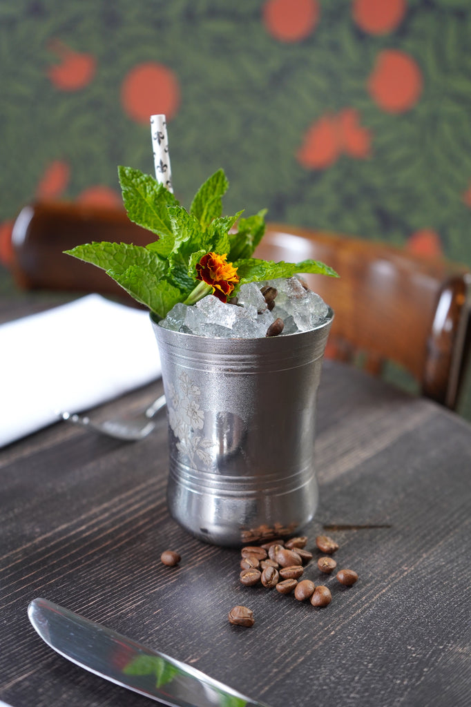 A chilled metal glass garnished with mint, marigold, and coffee beans