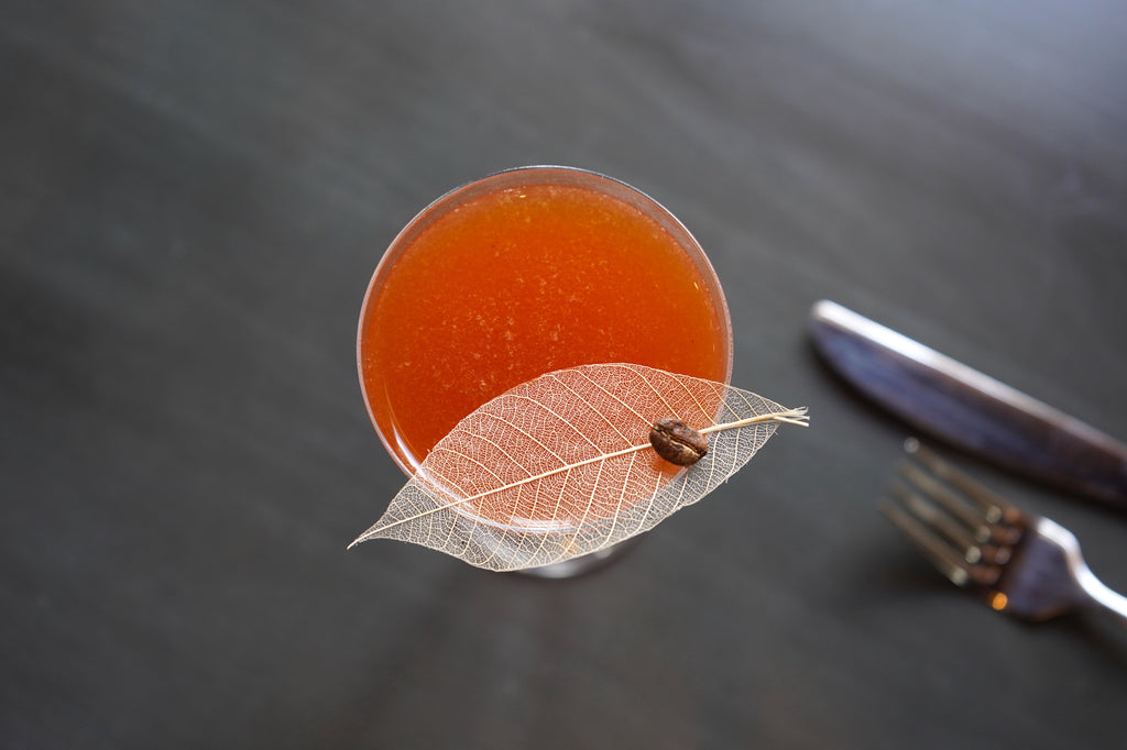 A coral orange-pink cocktail with a delicate garnish