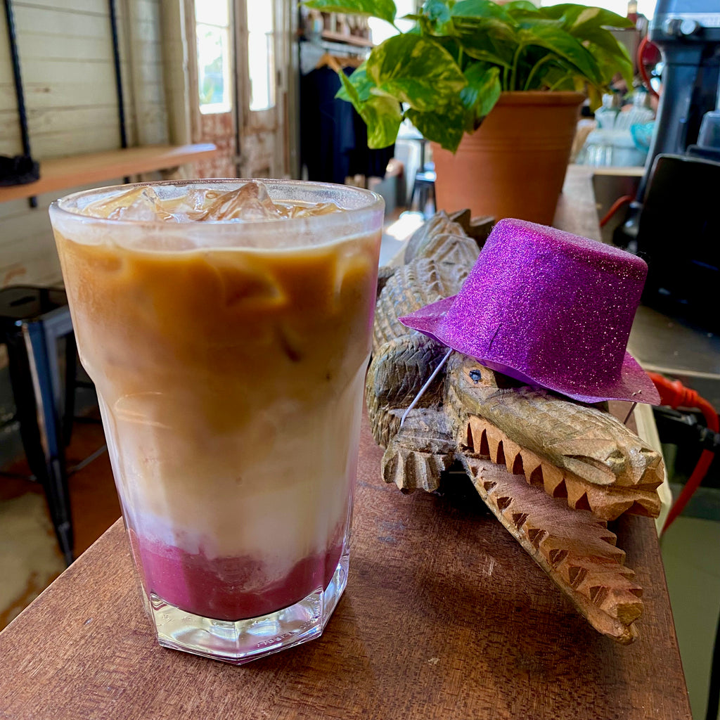 A layered, iced Ruby Latte next to a gator toy wearing a hat!