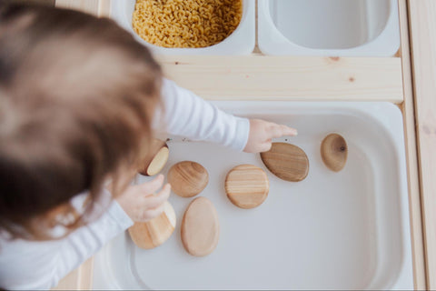 child playing with wooden circles in a bin