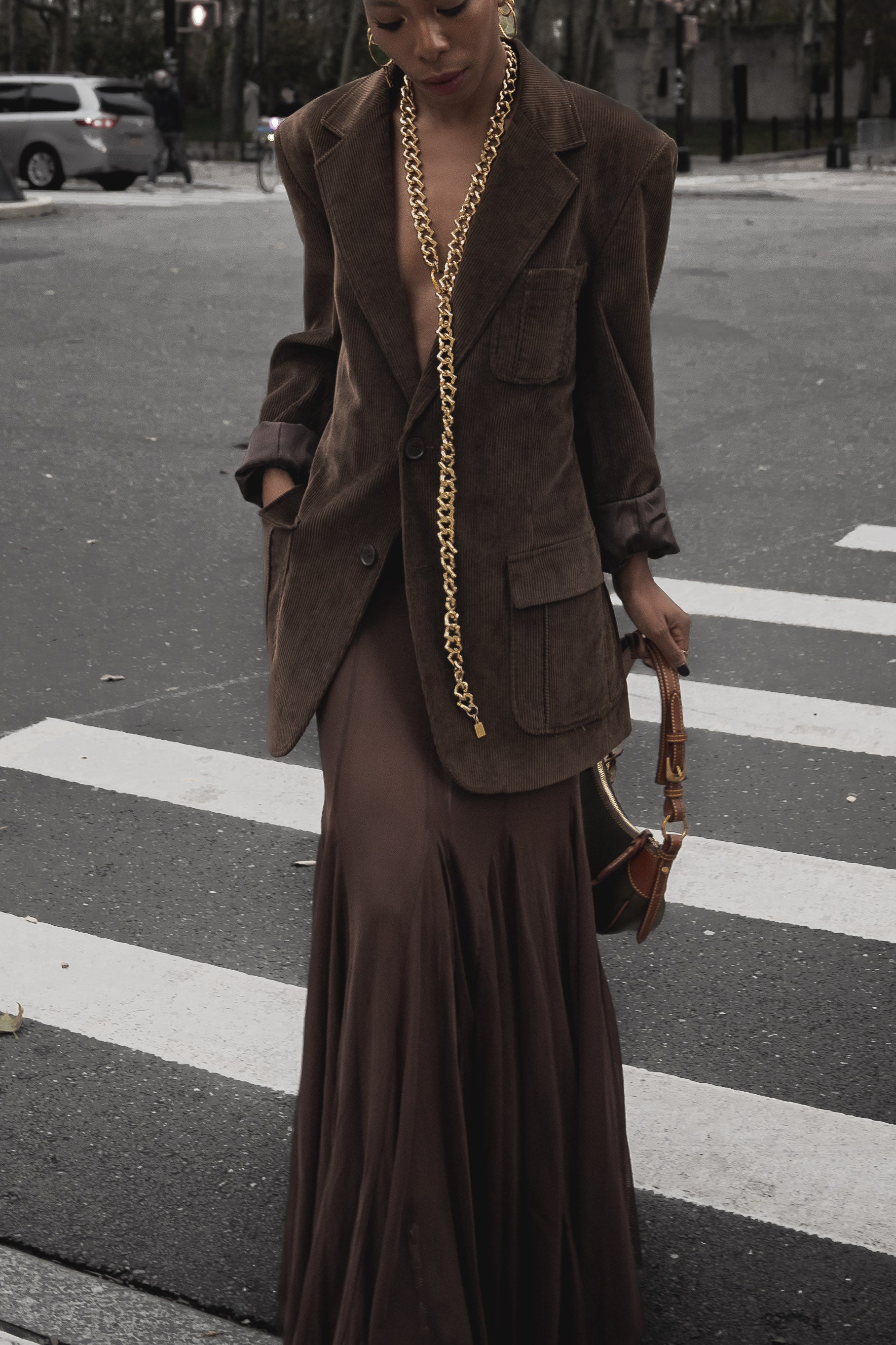 a photo of a woman on the street in NYC wearing a brown blazer, brown maxi skirt and gold long statement necklace