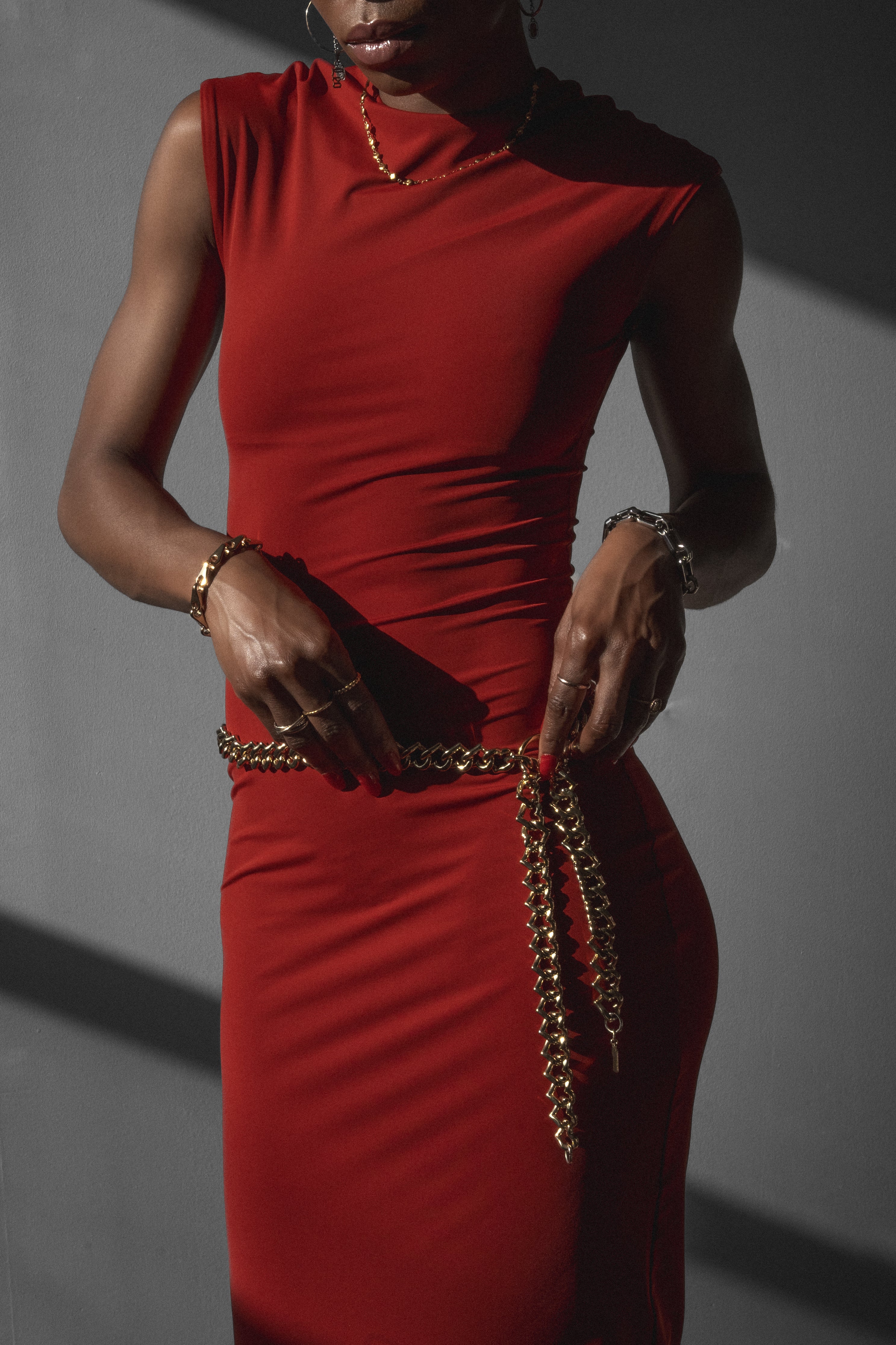Woman wearing red bodycon midi dress while putting on gold chain belt