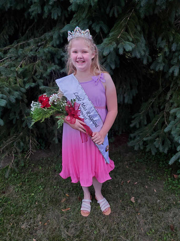 little girl wearing a sash and tiara from a pageant, holding a flower bouquet