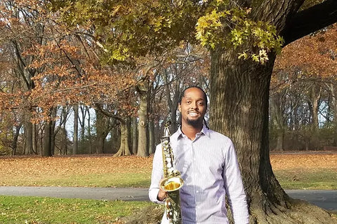 Carl Bartlett, Jr. holding saxophone outdoors in front of a tree - photo courtesy of Buzz B