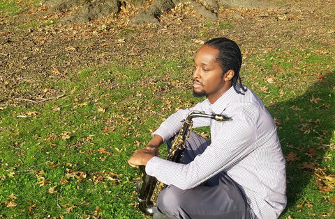 Award-winning Saxophonist Carl Bartlett, Jr. sitting with his saxophone in a meadow