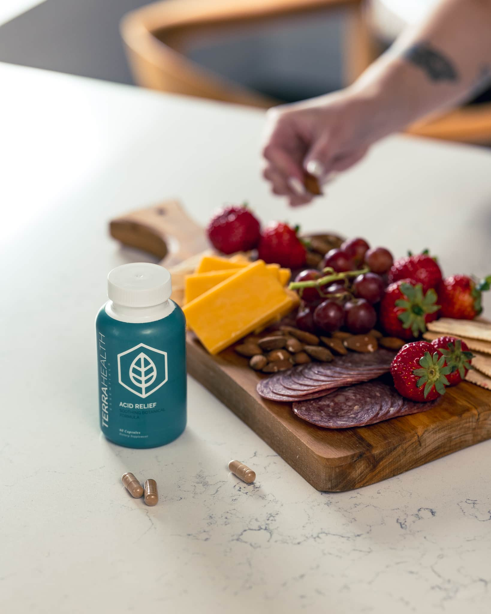 Bottle of acid relief capsules beside a charcuterie board with cheese, fruits, nuts, and salami.