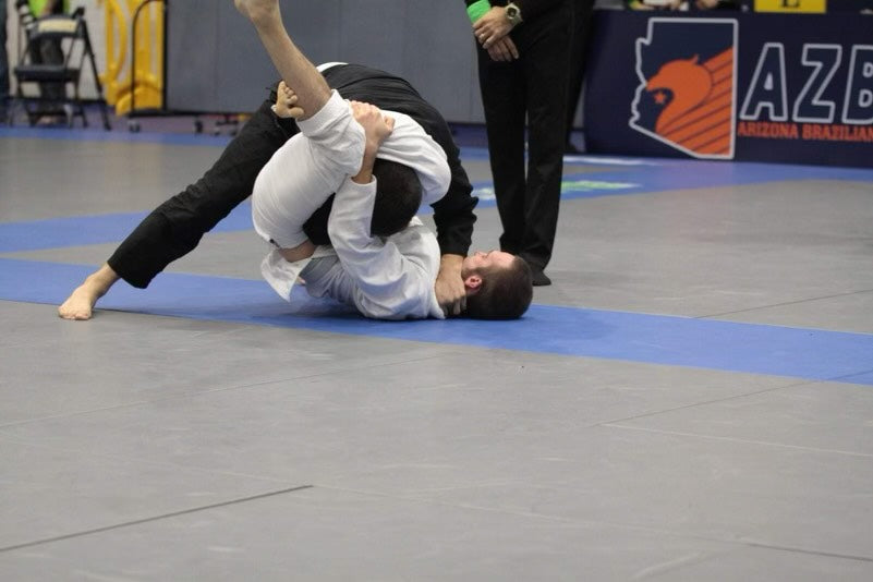 Two competitors in the middle of a BJJ match, competitor with the white gi/kimono executing a triangle choke