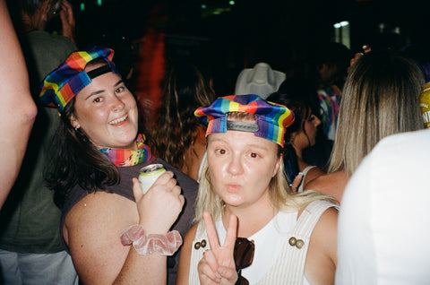 Two women at a festival wearing rainbow hats smiling to the camera taken on 35mm film