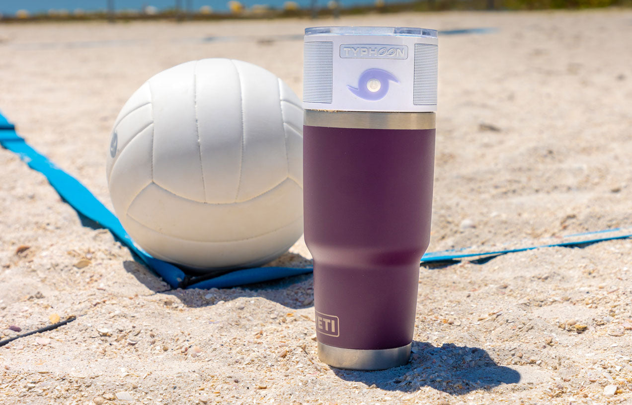 white typhoon speaker on large purple tumble situated in the sand next to a volleyball