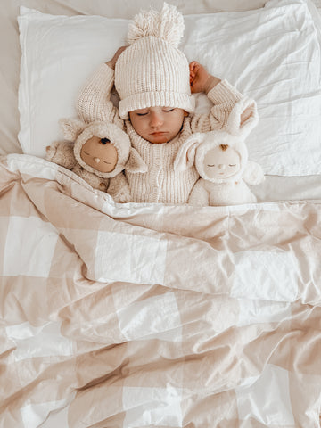 Baby sleeping in her crib with a Snuggly Jacks Sand Gingham Cot Quilt