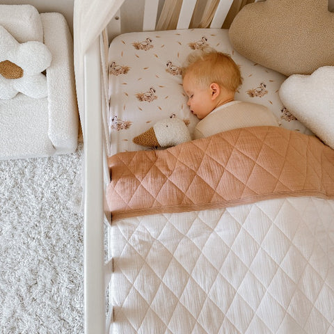 Adorable newborn laying under a snuggly jacks cotton coverlet.