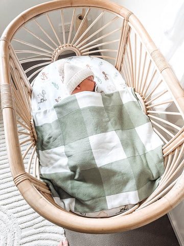 Newborn baby in a rattan bassinet with a Snuggly Jacks Sage Gingham Organic Knitted Blanket