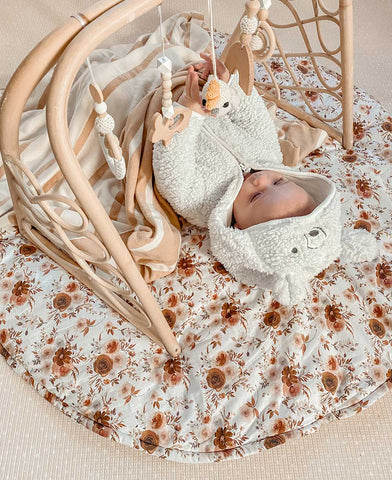 Small baby laying on a Snuggly Jacks Playmat with a wooden play gym overhead