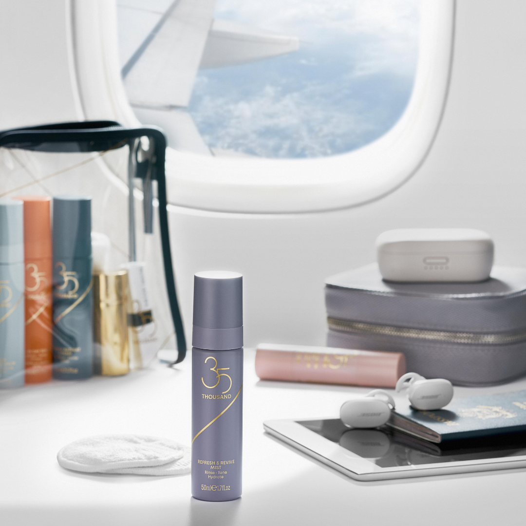 Refresh & Revive Mist near an airplane window. Includes earbuds, passport, ipad, and travel pouch. Clever Cleansing Balm, All-In Day Serum with SPF 30 and Really Radiant Cream inside Signature Clear Travel Bag.