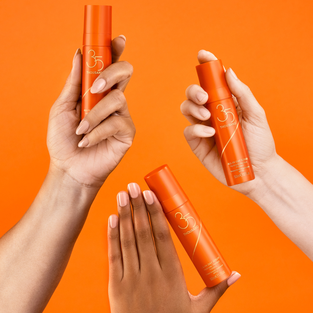 Three hands including fair, medium, and dark skin tones holding All-In Day Serum with SPF 30