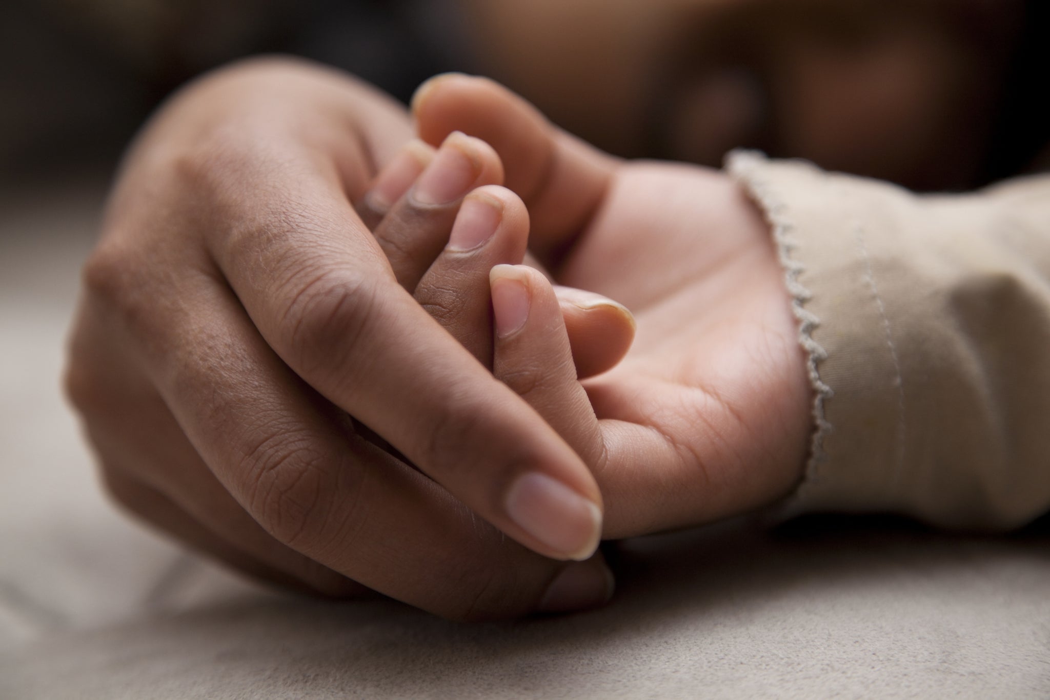 Adult hand holding baby's hand.