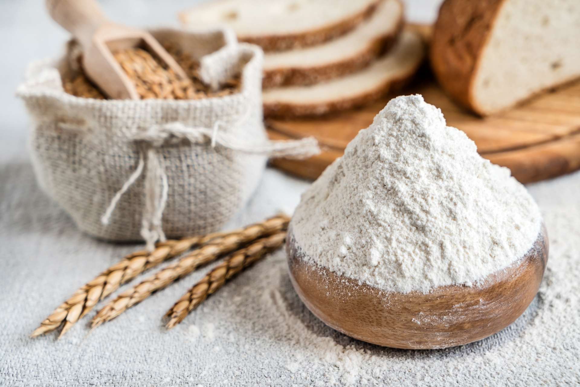 Bread flour in a bowl surrounded by wheat with bread in the background