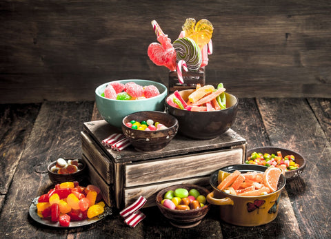 Assorted sweet candies, including jelly, marshmallows, and candied fruits, some arranged on a wooden palette with others scattered around it.