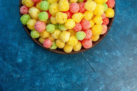 Half-shot of vibrant, colorful candies in a small brown pot, set against a bright blue background in a horizontal orientation.